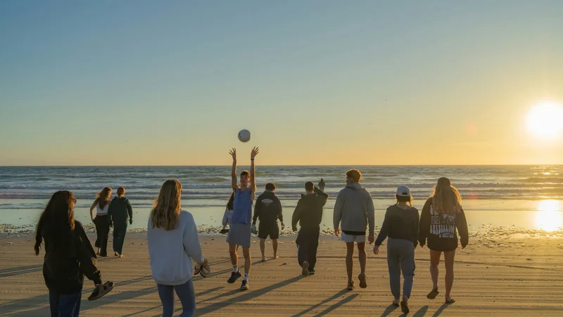 A group playing volleyball on the beach at sunset