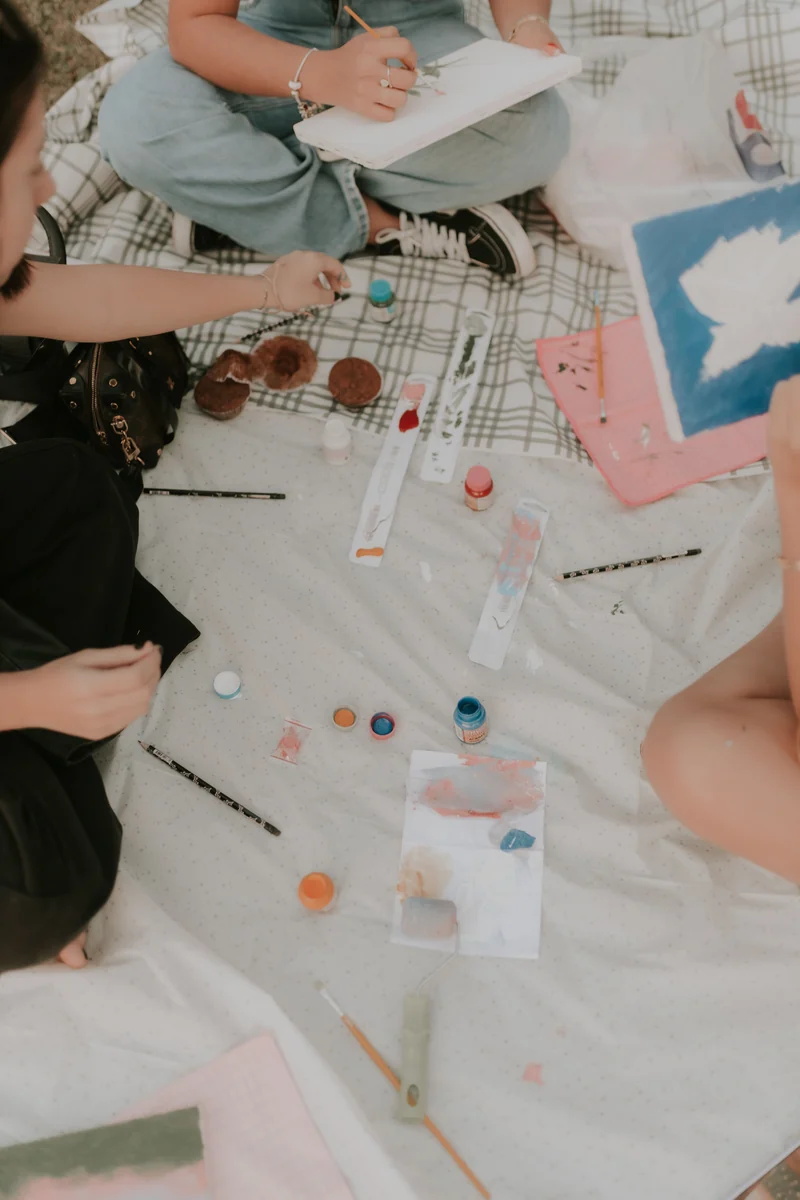 Friends painting with brushes and canvases together on a picnic blanket