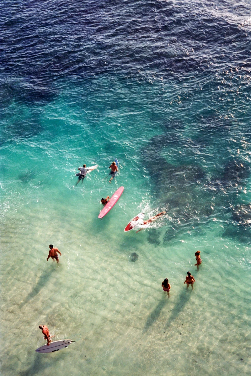 Surfers with colorful boards in clear turquoise water, seen from above