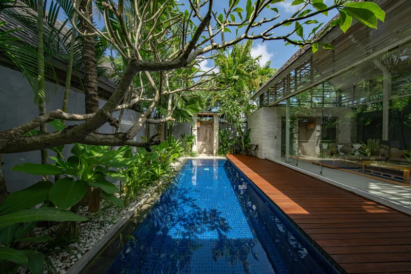 A long pool beside an open villa, framed by palms