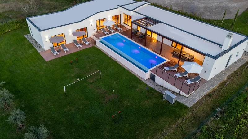 An Istrian house from above, with a pool and lawn surrounded by forest